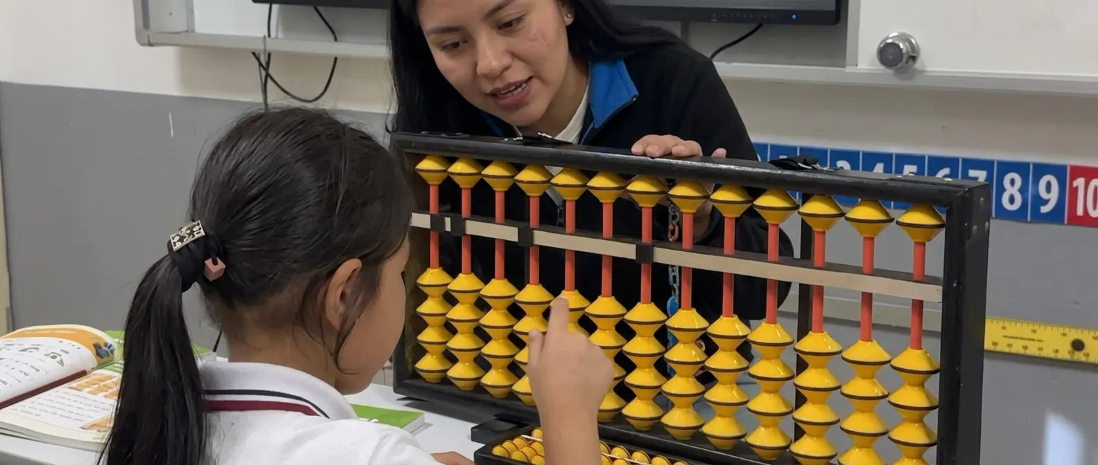 Teacher guiding a pupil on a large classroom abacus